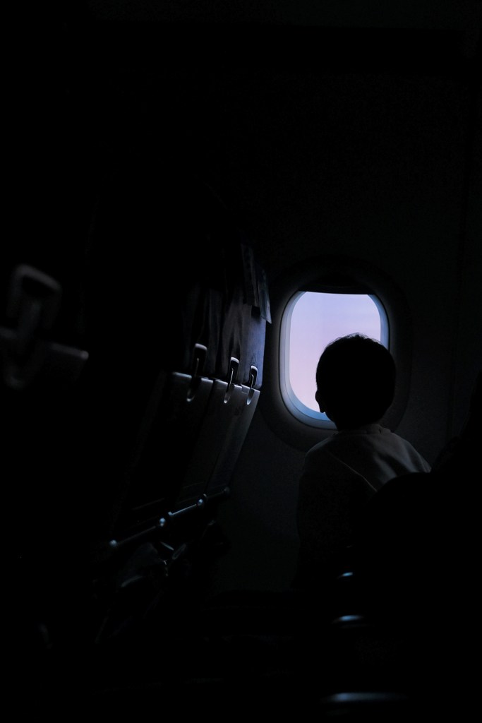Photo of a person's head in the dark inside of an airplane peering out the window