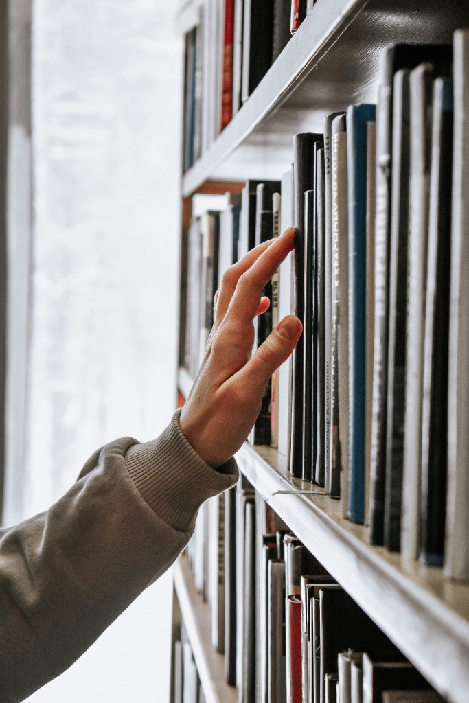 Photo of a bookcase with a woman's hand reaching up to the books