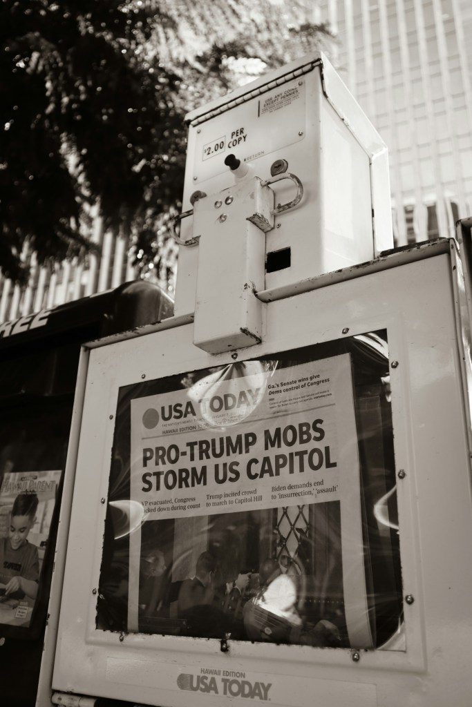 Photo of a newspaper box showing a newspaper with the headline: Pro Trump Mobs Storm US Capitol
