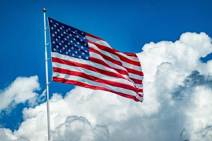 Photo of the US flag unfurled against a  blue sky with white puffy clouds