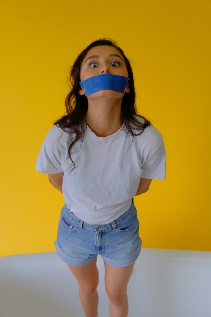 Photo of a young woman with blue tape across her mouth