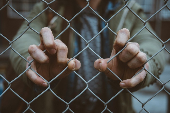 Photo of a man's hands grasping the wire fence he is being held behind.