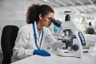 Photo of a woman in a white lab coat looking into a microscope.