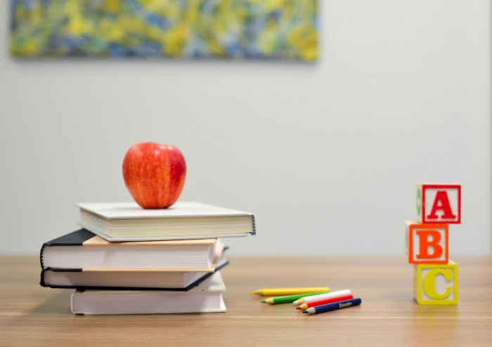 Photo of a stack of books with a red apple on top, with pencils lying beside the books and ABC blocks.