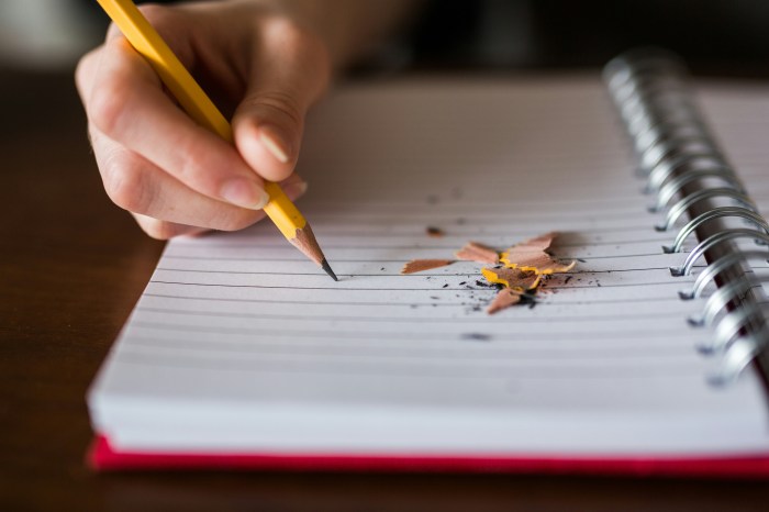Photo of a hand holding a pencil poised on a blank writing tablet